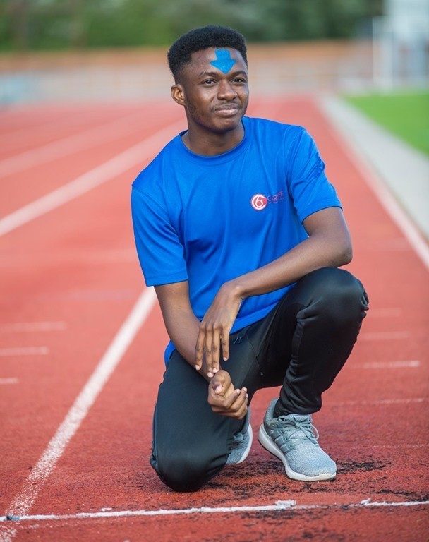 Smiling student kneeling down on the athletic track wearing a blue t-shirt